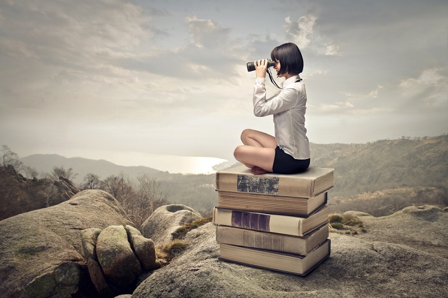 Jeune fille assise sur des livres qui regarde dans des jumelles